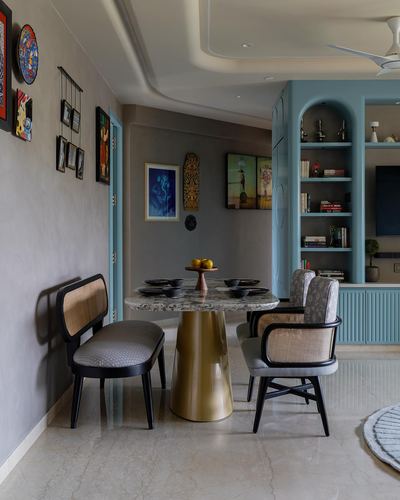 Dining nook with terrazzo table on brass base, cane chairs, and gallery wall beside a blue arched shelf unit