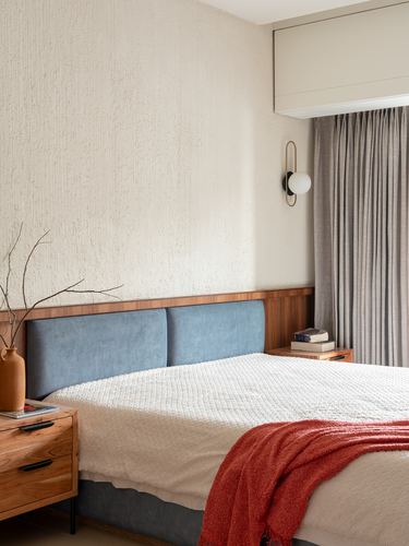 Bedroom with blue upholstered headboard, wood nightstands, textured plaster wall, and sconce lighting