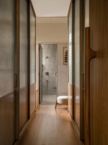 Wood-panelled wardrobe corridor leading to a tiled walk-in shower with a stool.