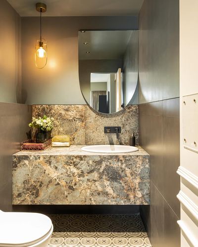Floating stone vanity with oval mirror, pendant light, and patterned floor tile in a compact bathroom