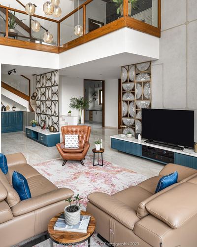 Double-height living room with teal TV console, carved wood panels, and beige sectional sofa
