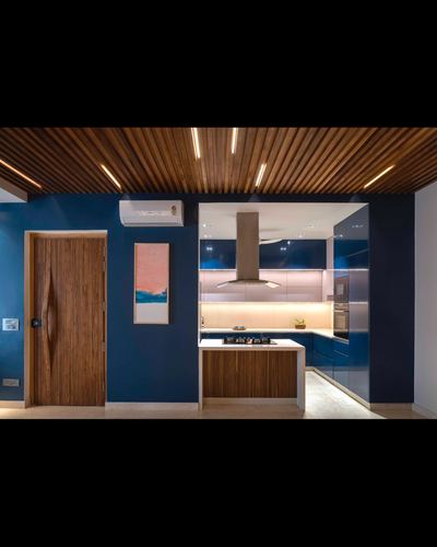 Blue lacquered kitchen with wood-slatted ceiling, chimney hood, and sculpted wooden pivot door