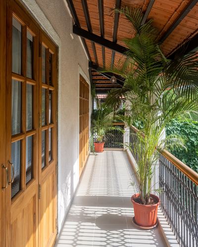 Sunlit covered veranda with wooden doors, terracotta ceiling, iron railing and potted palms