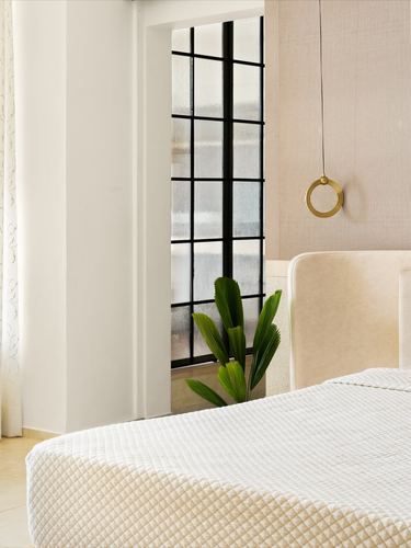 Bedroom corner with fluted wall, crittall window, plant, and quilted bed