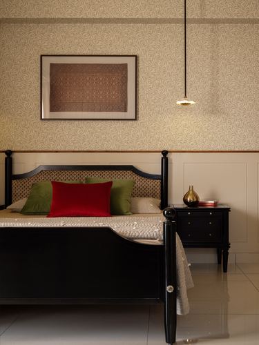 Dark wood four-poster bed with red and green cushions beneath framed textile art on patterned wallpaper