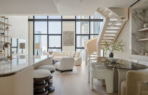 Open-plan cream living and dining area with floating staircase, marble wall, and curved boucle sofa