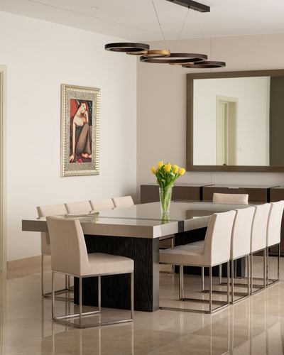 Minimalist dining room with long glass-top table, cream chairs, and cluster pendant light fixture
