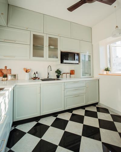 Sage green L-shaped kitchen with black and white checkerboard floor and fluted glass cabinets