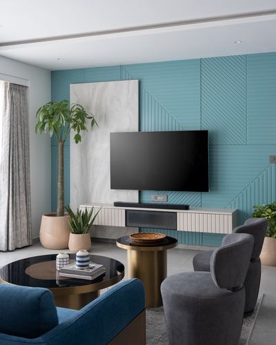 Living room with fluted teal accent wall, wall-mounted tv, round brass coffee tables and grey chairs