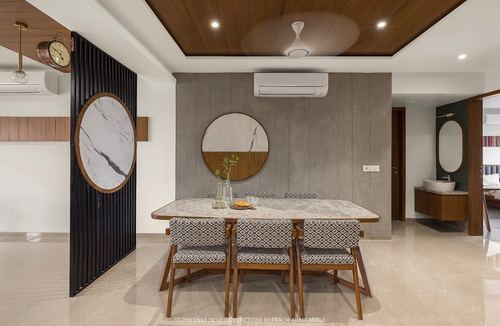 Dining room with marble table, patterned chairs, and round wood-framed mirror on grey wall