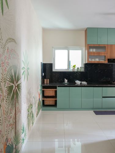 Sage-green modular kitchen with black granite backsplash beside a botanical mural wall