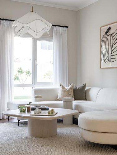 Minimalist white living room with curved sofa, round stone coffee table, and pleated pendant light