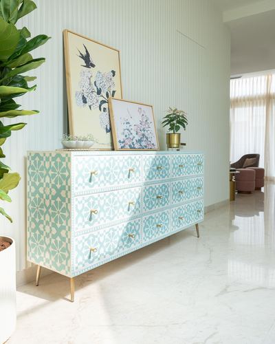 Turquoise and white patterned sideboard with brass legs against ribbed white wall in bright hallway