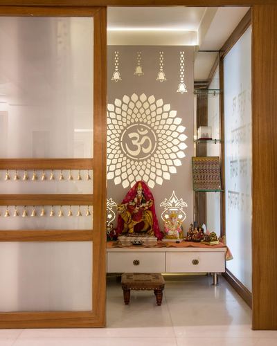 Pooja unit with om symbol wall cutout, deity idols, brass bells, viewed through sliding glass door