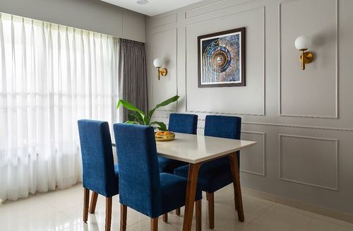 Dining room with navy chairs, white marble table, paneled grey walls and brass sconces
