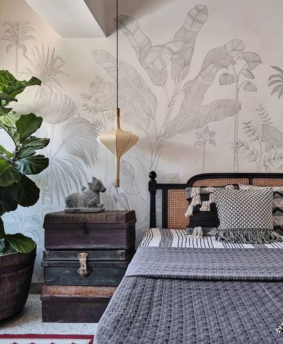 Bedroom with cane headboard, stacked vintage trunks, and botanical mural wallpaper
