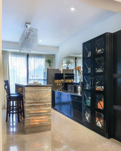 Kitchen island in beige stone lit from within, facing black glass cabinetry wall and crystal chandelier