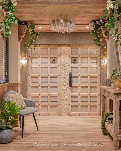 Carved wooden double door entrance with brass studs, sconces, chandelier and cane armchair