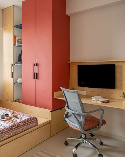 Study nook with red wardrobe, wall-mounted tv on plywood desk, and grey office chair