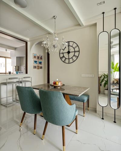 Dining nook with teal velvet chairs, marble table, chandelier and oversized wall clock