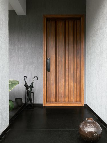 Entry foyer with ribbed wooden door, dark stone floor, ceramic vase and umbrella stand