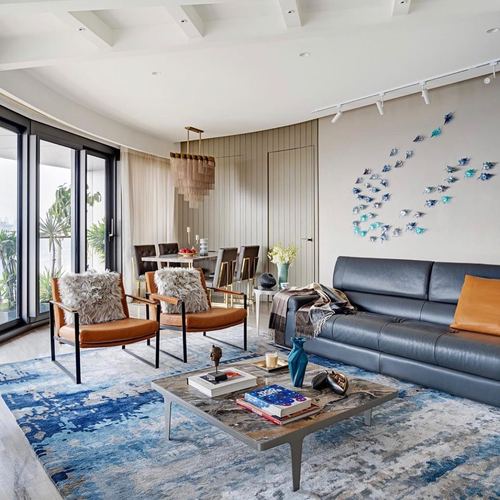 Living room with curved windows, navy leather sofa, tan chairs and fish wall art