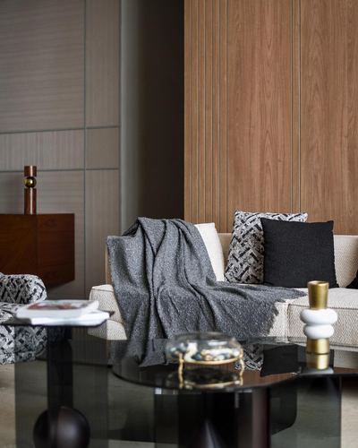 Sofa with grey throw and patterned cushions against wood-paneled wall, glass table in foreground