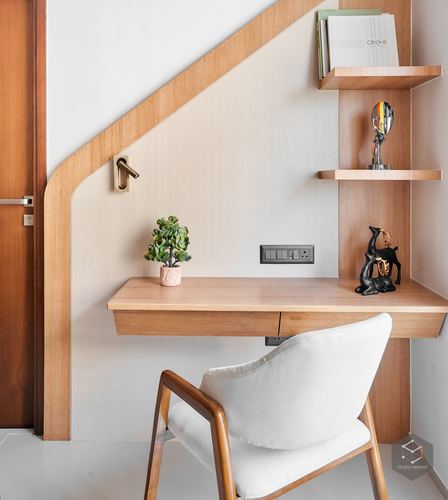 Built-in wooden study desk under angled staircase with floating shelves and cane-back chair