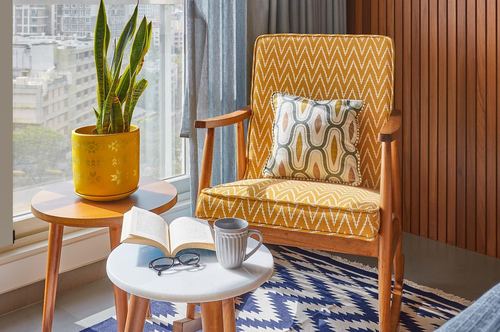 Mustard chevron armchair with patterned cushion beside marble-top side tables near window, city view behind