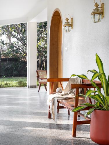 Covered veranda with terrazzo floor, wooden bench, arched wood doorway and garden view