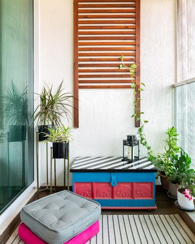 Balcony corner with wooden louvered wall panel, painted trunk, lantern, plants and floor cushions