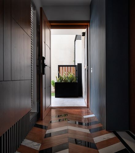 Entrance corridor with patterned wood-and-stone floor leading through an open door to a courtyard planter.