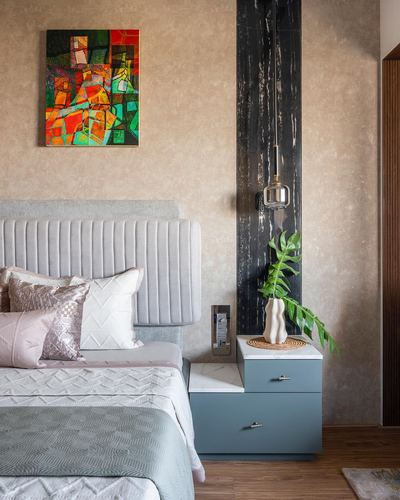 Bedroom with channel-tufted grey headboard, blue two-tier nightstand, and black textured pillar with pendant light