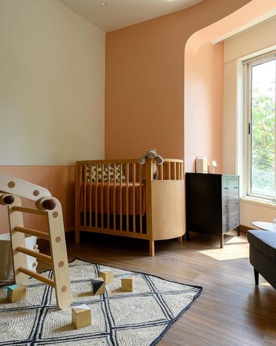 Nursery with round wooden crib in arched terracotta alcove and pikler triangle on rug