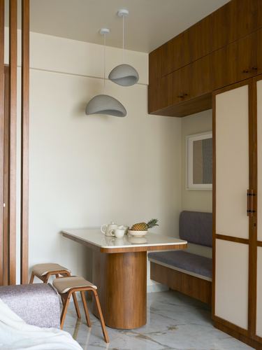 Compact dining nook with curved wooden pedestal table, upholstered bench, and dome pendant lights