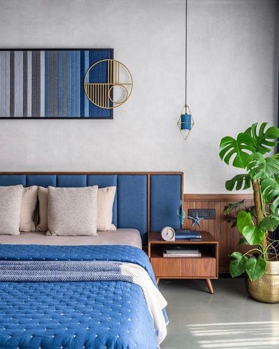 Blue upholstered bed with wood nightstand, pendant light, and monstera plant against grey wall