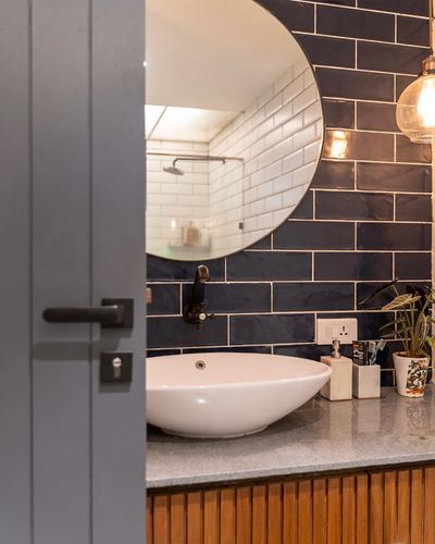 View through open door into bathroom with navy tiled wall, round mirror, and vessel sink