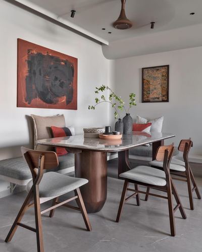 Dining room with marble-top table, wooden chairs, banquette seating and abstract red-black painting on wall