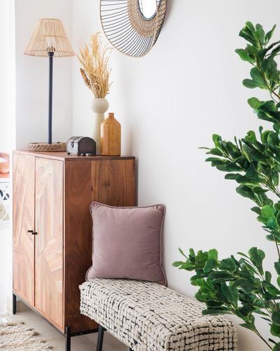 Wooden herringbone cabinet with rattan lamp, mirror, mauve pillow, woven bench and plant
