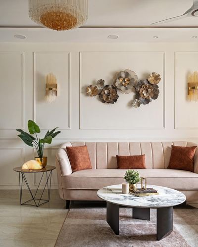 Blush velvet channel-tufted sofa with terracotta cushions beneath a metal flower wall sculpture, round marble coffee table in front