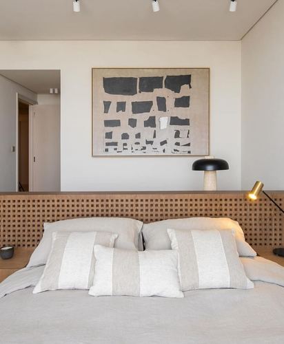 Bedroom with woven wood lattice headboard, abstract framed art, and layered linen pillows