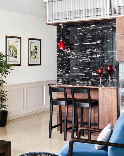 Home bar with black marble backdrop, wood stools, red pendant light and blue armchair in foreground