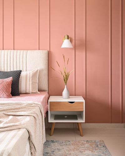 Bedside table with vase beside cream bed against pink panelled wall