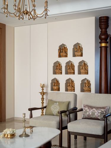 Living room wall with arched niches holding brass deity figures above two armchairs