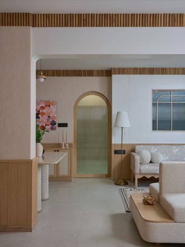Living room with arched fluted wood doorway, boucle sofa, and pink plaster column
