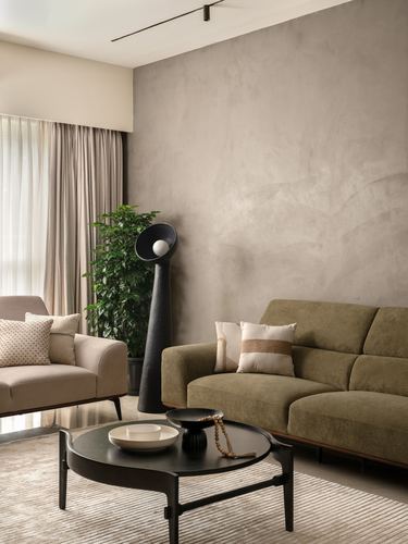 Living room with olive sofa, black round coffee table, and textured grey plaster wall
