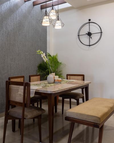 Dining nook with stone-top table, cane chairs, bench, geometric pendant lights, and large round wall clock.