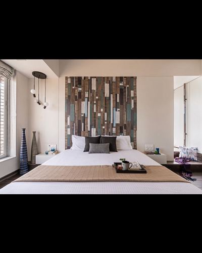 Bedroom with king bed, patchwork wood headboard, cluster pendant lights, and window seat