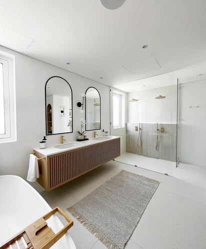 White bathroom with fluted wood vanity, arched mirrors, freestanding tub, and glass walk-in shower