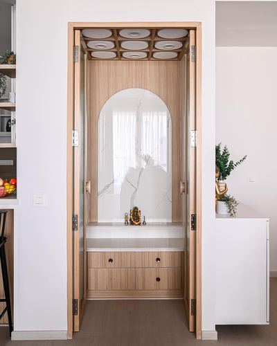 Compact pooja unit with arched stone niche, wooden folding doors, and ceiling light coffers